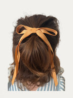 Classic long grosgrain bow clip for girls in Curry; warm tone, elegant silhouette, made in Spain and shipped from Switzerland.